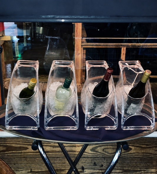 Four wine bottles in clear ice buckets on a metal tray with a dark background.