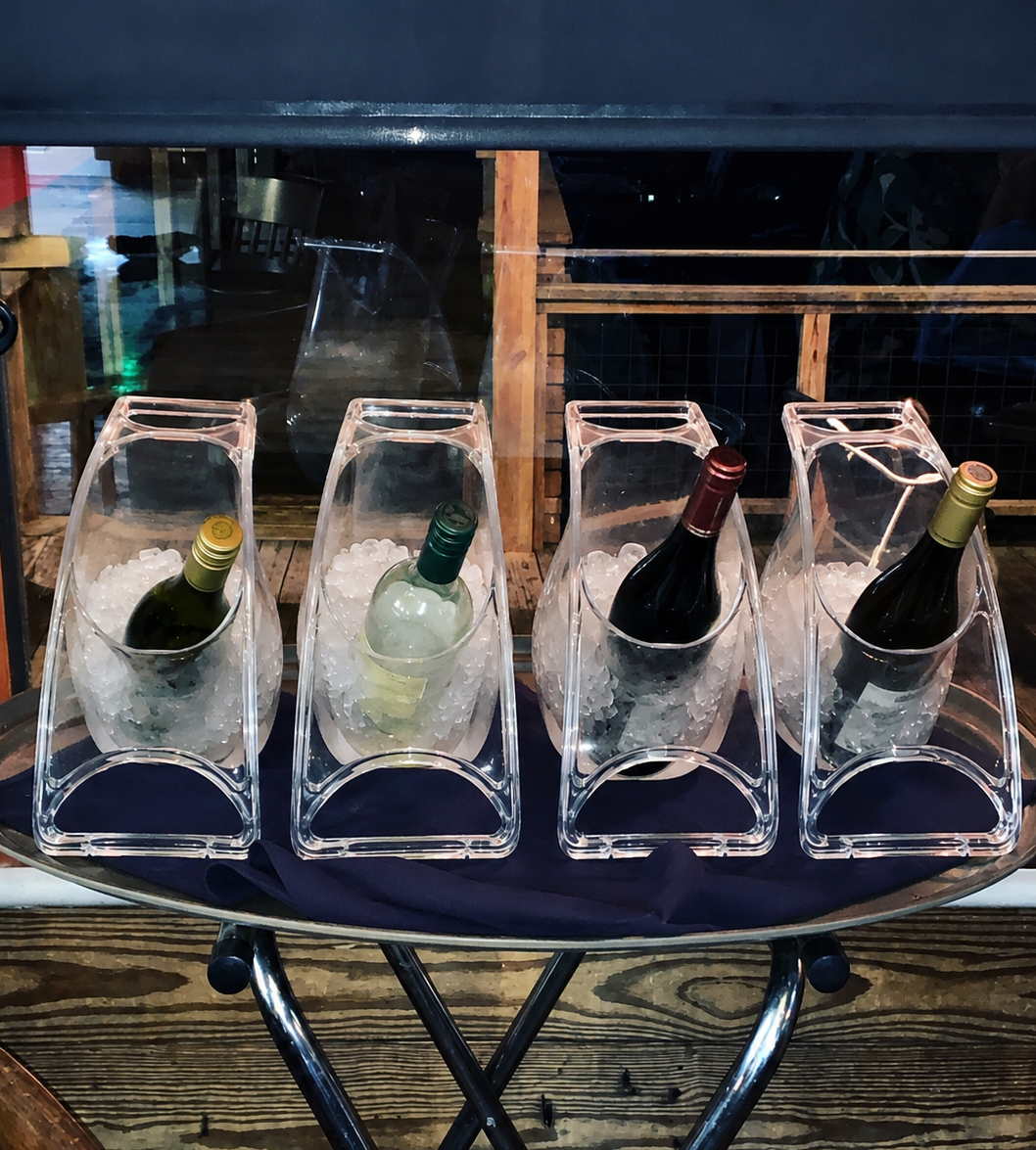 Four wine bottles in clear ice buckets on a metal tray with a dark background.